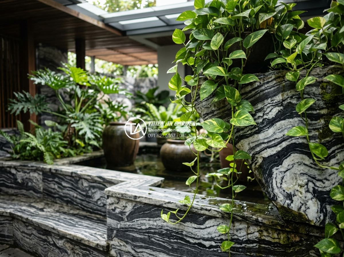 7 Loại cây trồng giếng trời ít ánh sáng cực dễ chăm sóc - Pothos vines gracefully draping over natural stone edges in a shaded Vietnamese 