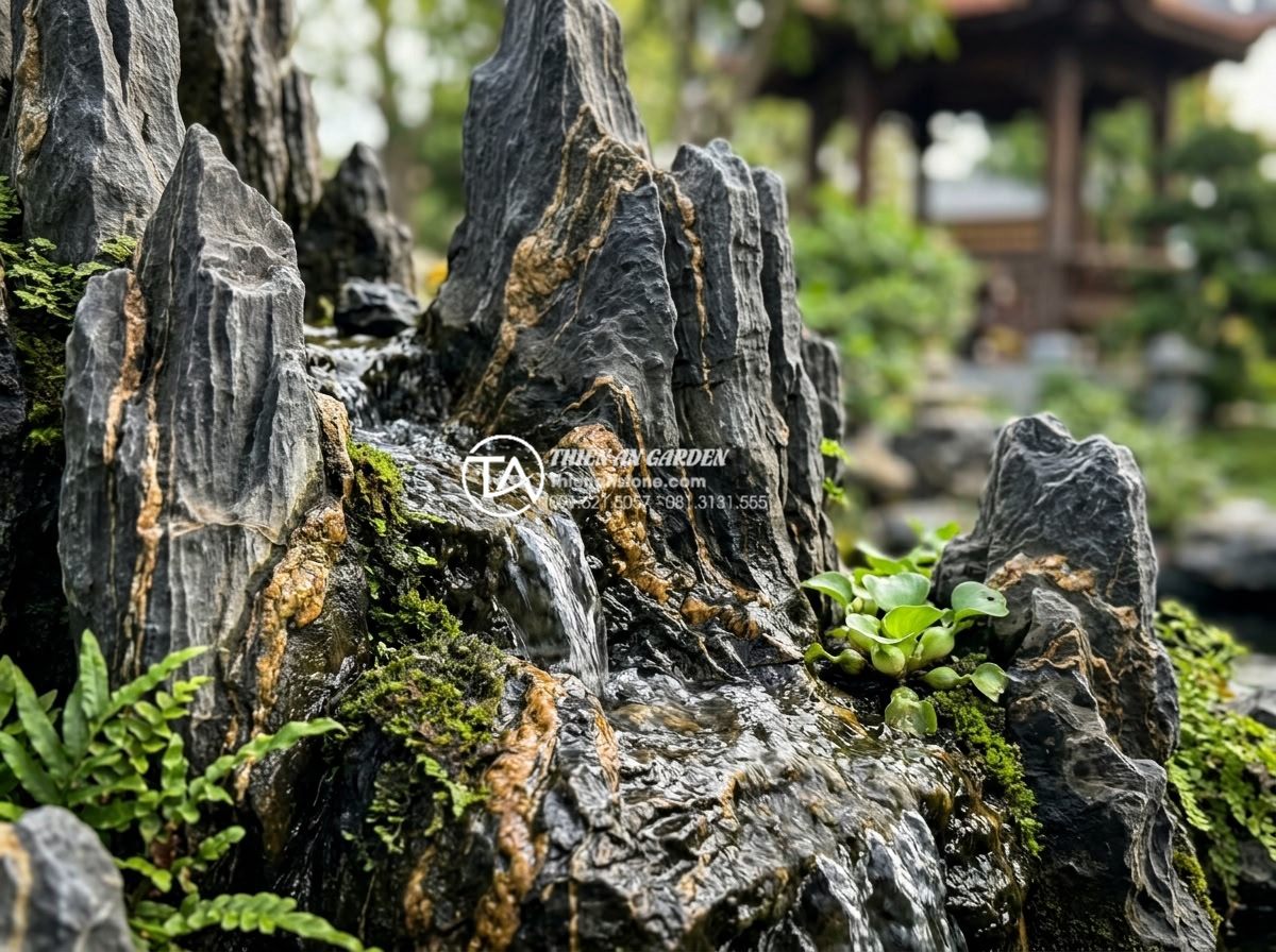 So sánh tiểu cảnh bể cá ngoài trời và bể cá trong nhà: Lựa chọn nào tối ưu? - Hình 4 So sánh tiểu cảnh bể cá ngoài trời và bể cá trong nhà: Lựa chọn nào tối ưu? - Close-up of natural stone waterfall detail in outdoor Koi pond showing water flo