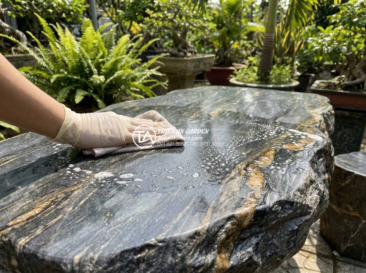 Bàn ghế đá hoa cương (Granite): Đặc điểm, ưu điểm và các mẫu bền đẹp nhất - Hình 11 Bàn ghế đá hoa cương (Granite): Đặc điểm, ưu điểm và các mẫu bền đẹp nhất - Close-up of person gently cleaning a polished granite outdoor table with soft cl