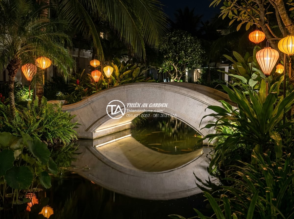 Cầu trang trí sân vườn bằng đá tự nhiên: Ưu điểm vượt trội so với gỗ và bê tông - Hình 9 Cầu trang trí sân vườn bằng đá tự nhiên: Ưu điểm vượt trội so với gỗ và bê tông - Stunning nighttime view of an illuminated natural stone garden bridge with subtl