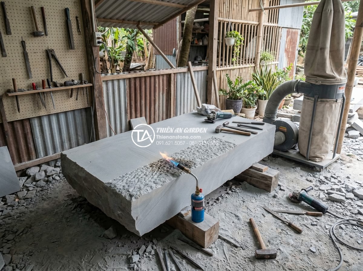 Sự khác biệt giữa đá Granite và đá Cẩm Thạch khi chế tác cầu sân vườn - Artisan workshop scene showing skilled craftsmen hand-finishing a large granite 