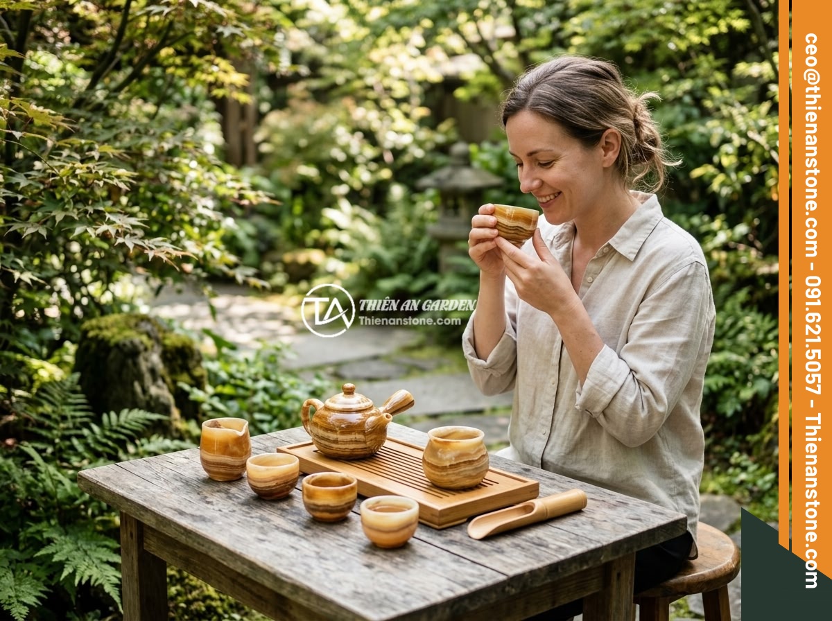 Hướng dẫn vệ sinh ấm chén đá đúng cách tránh làm hỏng bề mặt đá - A person enjoying tea from a well-maintained natural stone tea set in a serene g