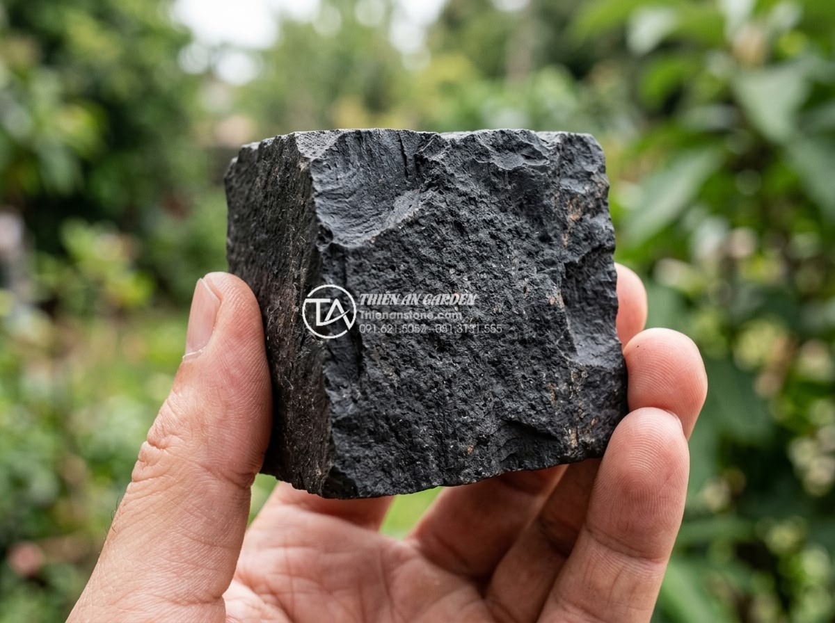 Đá Cubic Bazan Đen Chẻ Thô - Chất liệu: Đá bazan đen tự nhiên (Gia Lai/Bình Định) - Kích thước: 10x10x5cm hoặc 10x10x8cm (dày 5-10cm) - Hình 3 Đá Cubic Bazan Đen Chẻ Thô - Chất liệu: Đá bazan đen tự nhiên (Gia Lai/Bình Định) - Kích thước: 10x10x5cm hoặc 10x10x8cm (dày 5-10cm) - Close-up detailed texture of single 10x10x8cm black basalt cubic rough split sto