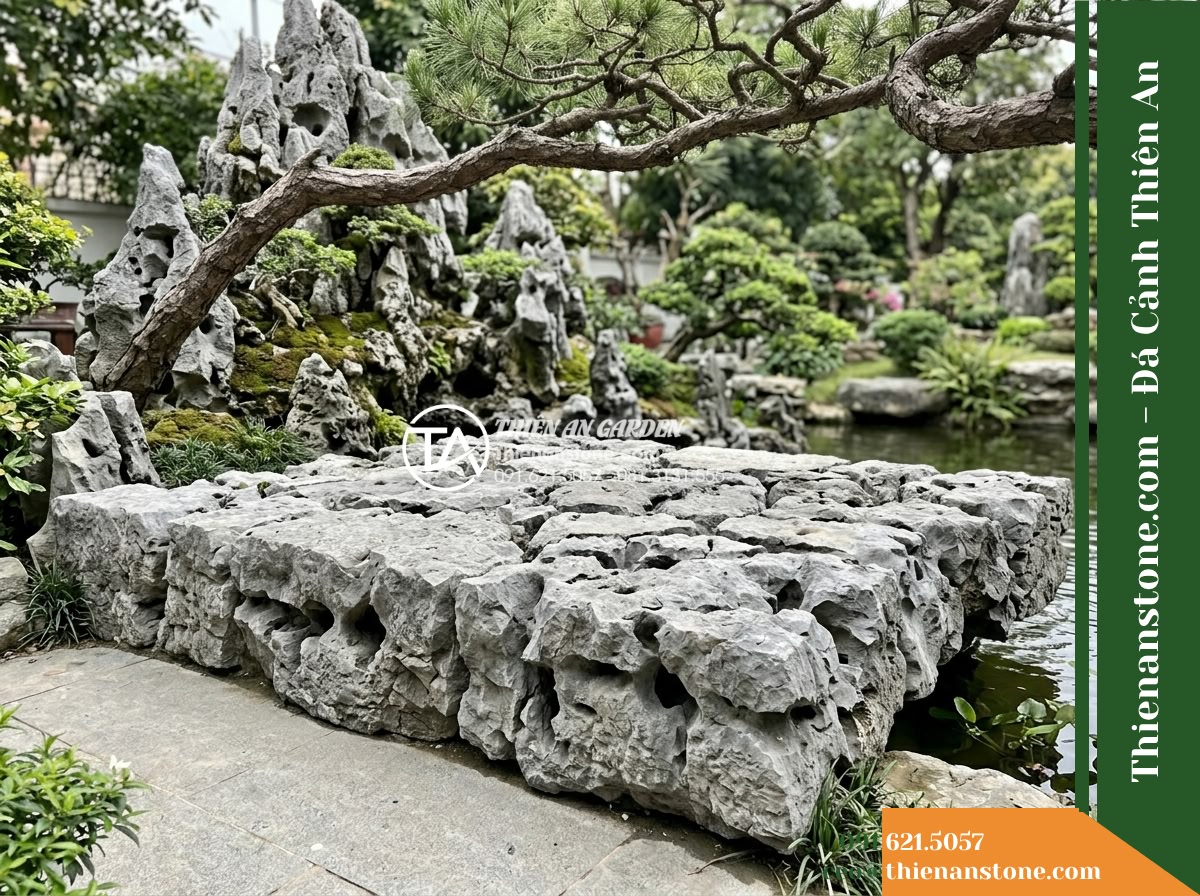 Đá Mão Xám (Khối trung 60–120cm / ~300–900kg) | Chuyên ghép bệ móng vững chãi, tạo thềm đá phẳng sát mặt nước. - Hình 14 Đá Mão Xám (Khối trung 60–120cm / ~300–900kg) | Chuyên ghép bệ móng vững chãi, tạo thềm đá phẳng sát mặt nước. - View from a garden pathway looking towards the horizontal stone platform at the
