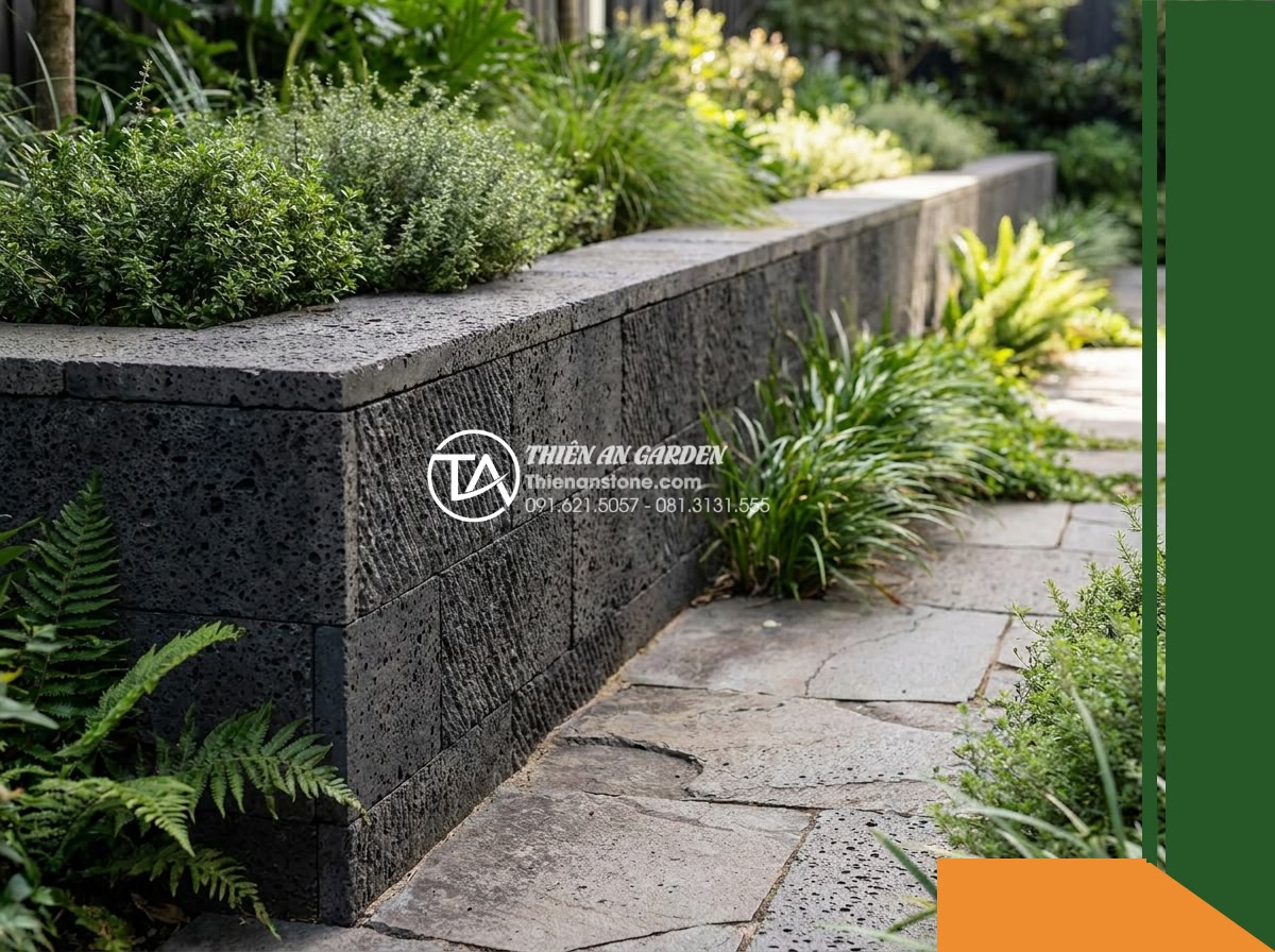 Đá răng lược đen tổ ong Đồng Nai | Bazan lỗ Đồng Nai | 10x50 cm - Hình 2 Đá răng lược đen tổ ong Đồng Nai | Bazan lỗ Đồng Nai | 10x50 cm - Perspective view along an outdoor garden walkway with a retaining wall clad in d