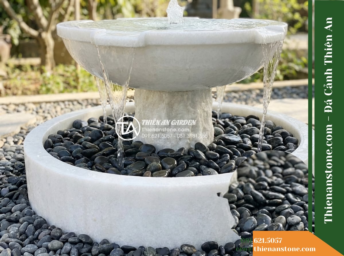Đài Phun Bát Tròn Chân Trụ Thô, Bát D90cm Cao 80cm - Hình 8 Đài Phun Bát Tròn Chân Trụ Thô, Bát D90cm Cao 80cm - A low-angle exterior shot focusing on the fountain base surrounded by dark tumbl