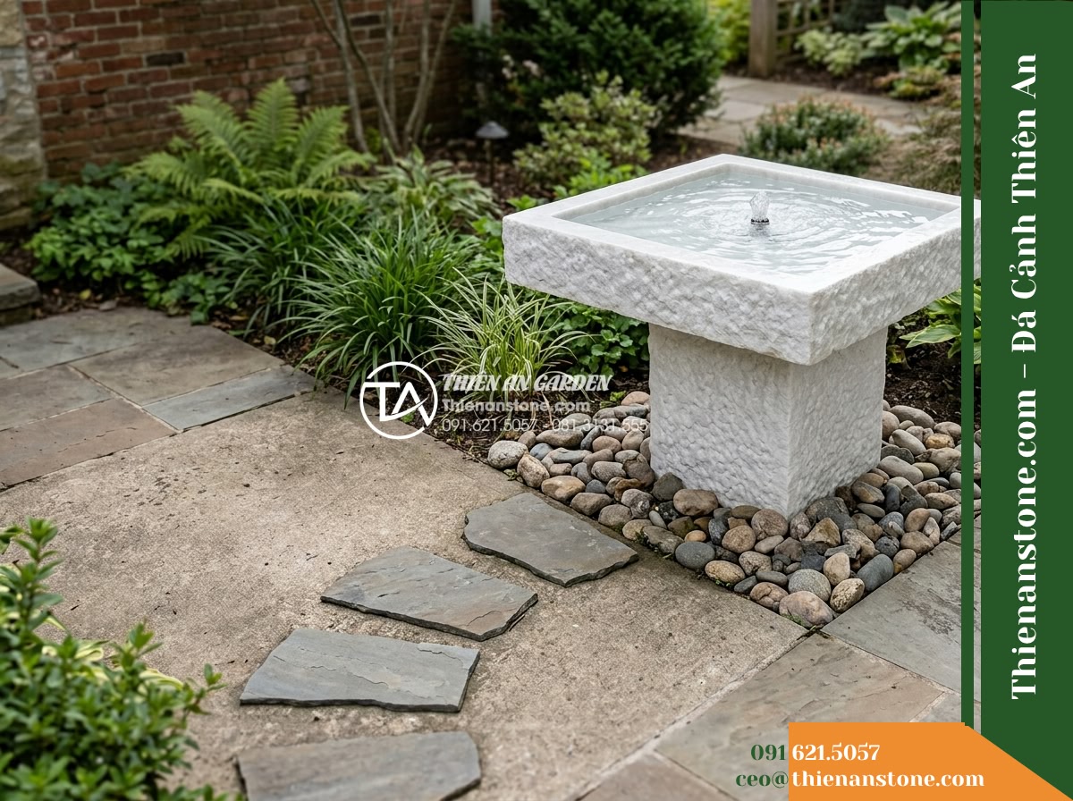 Đài Phun Bát Vuông Lòng Mài Mịn Vỏ Thô, Bát D80cm Cao 75cm - Hình 10 Đài Phun Bát Vuông Lòng Mài Mịn Vỏ Thô, Bát D80cm Cao 75cm - Secondary angle showing the square stone fountain offset on a patio corner with
