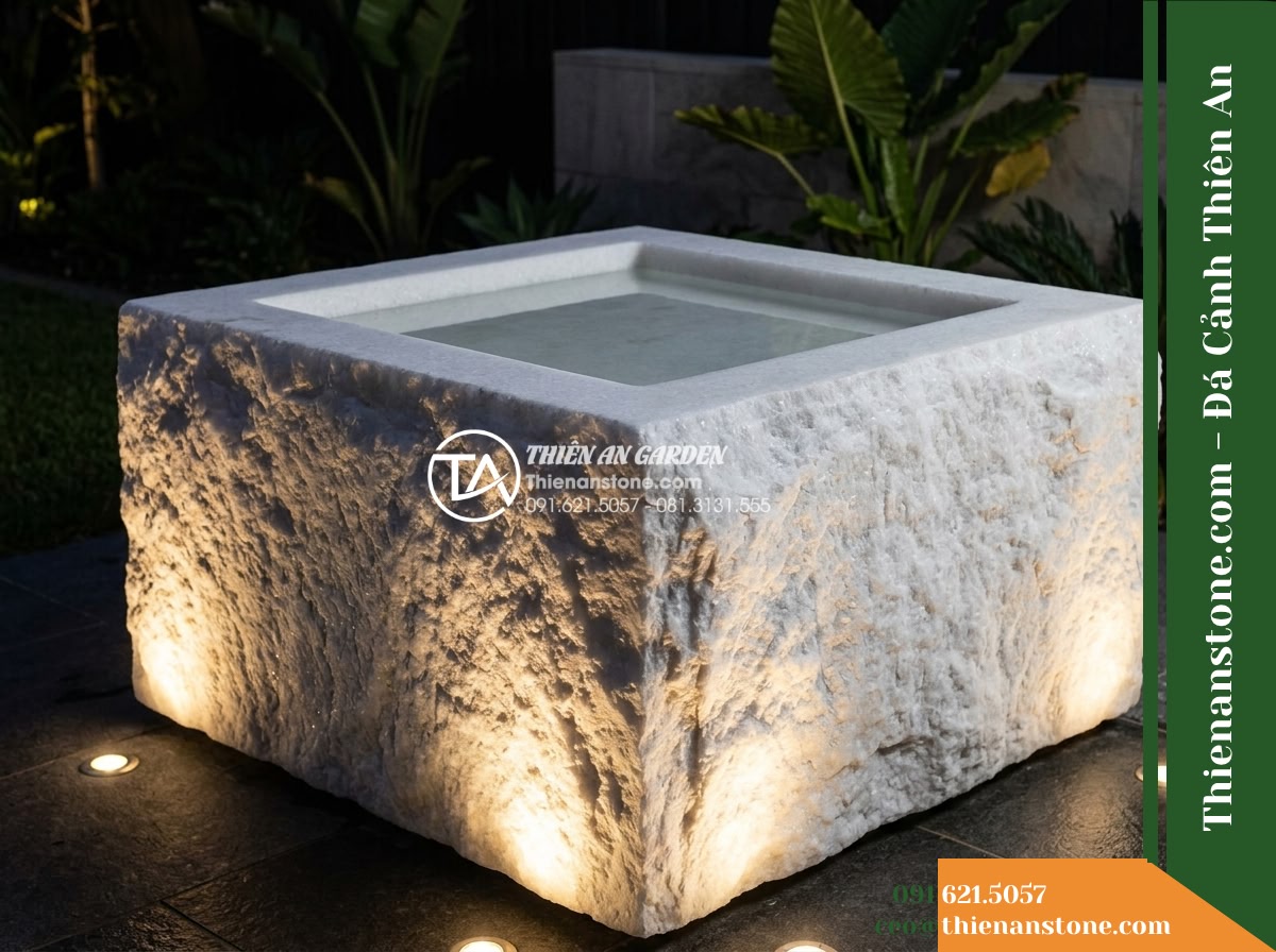 Đài Phun Bát Vuông Lòng Mài Mịn Vỏ Thô, Bát D80cm Cao 75cm - Hình 14 Đài Phun Bát Vuông Lòng Mài Mịn Vỏ Thô, Bát D80cm Cao 75cm - Nightscape shot of the square fountain illuminated by warm ground-level uplights