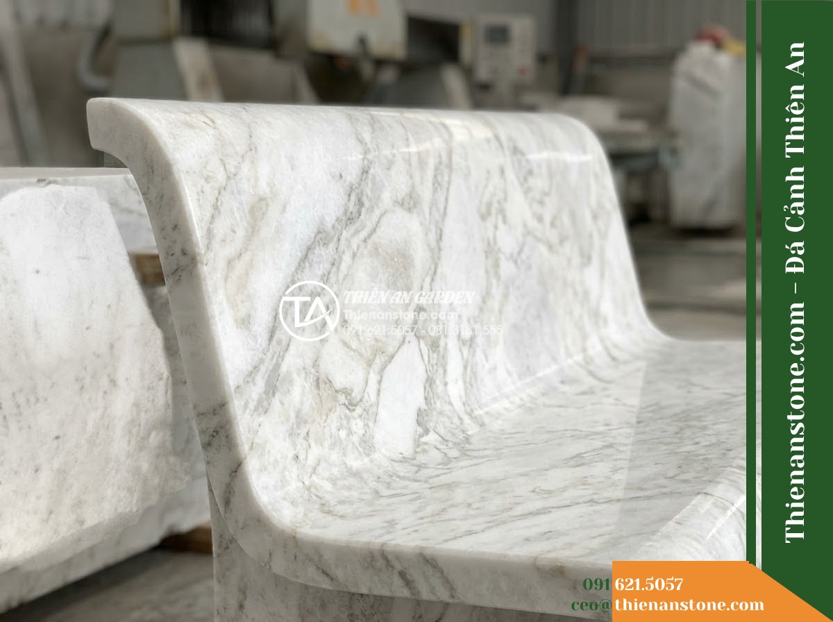 Ghế Đá Công Viên Có Tựa Cong Huyền Vũ 150x50x85cm - Đá Đen Cẩm Thạch - Hình 2 Ghế Đá Công Viên Có Tựa Cong Huyền Vũ 150x50x85cm - Đá Đen Cẩm Thạch - A beautifully crafted black marble stone bench under a large banyan tree, dapple