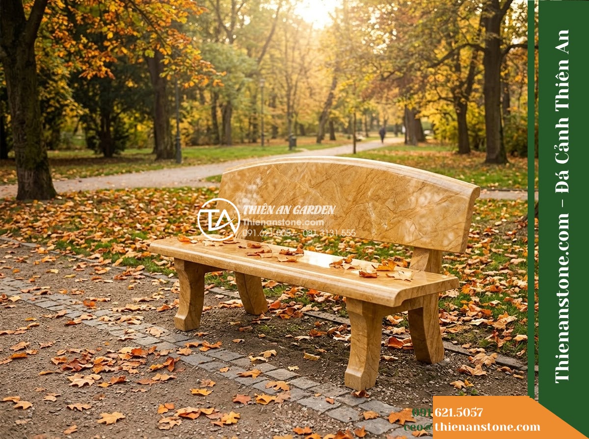 Ghế Đá Công Viên Có Tựa Vòm Cung Nhật Hạ 160x50x88cm - Đá Vàng Cẩm Thạch - Hình 3 Ghế Đá Công Viên Có Tựa Vòm Cung Nhật Hạ 160x50x88cm - Đá Vàng Cẩm Thạch - Autumn scene with fallen leaves scattered on a golden marble stone bench in a pe