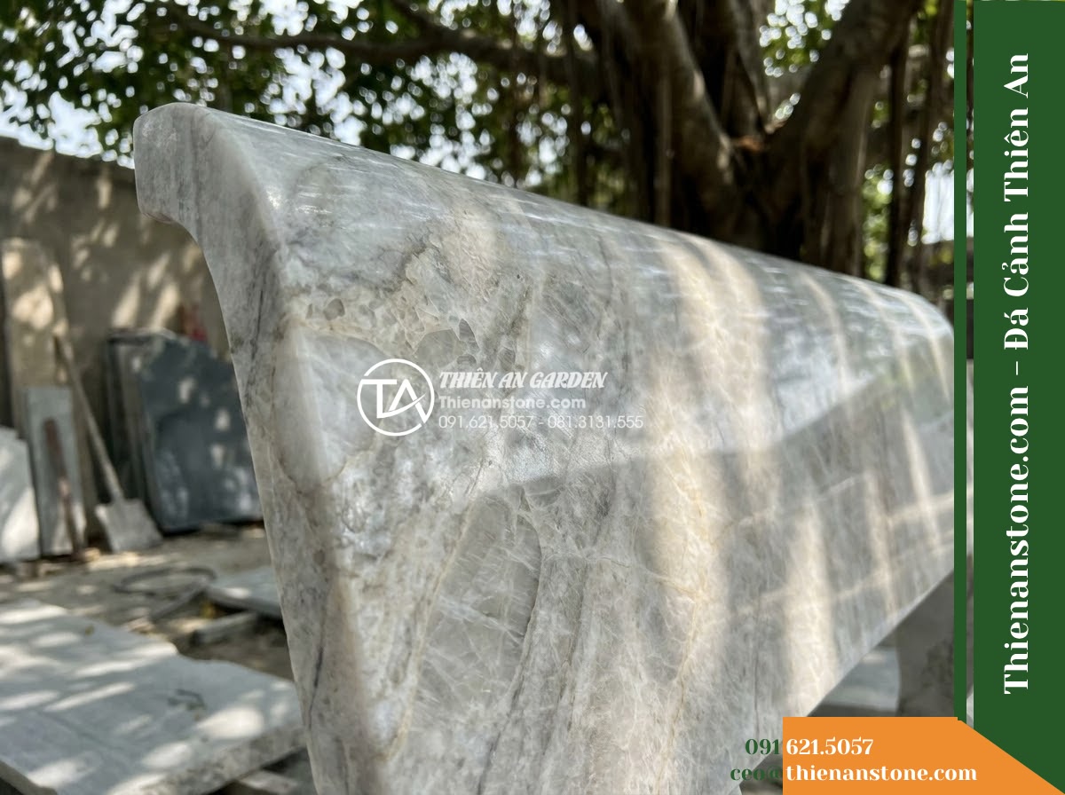 Ghế Đá Granito Hoàng An – Kích thước 160 x 50 x 83 cm – Kiểu dáng tựa vòm cao, chân bo mềm. Chất liệu đá granito (đá mài) - Hình 2 Ghế Đá Granito Hoàng An – Kích thước 160 x 50 x 83 cm – Kiểu dáng tựa vòm cao, chân bo mềm. Chất liệu đá granito (đá mài) - A beautifully crafted granito polished stone stone bench under a large banyan tr