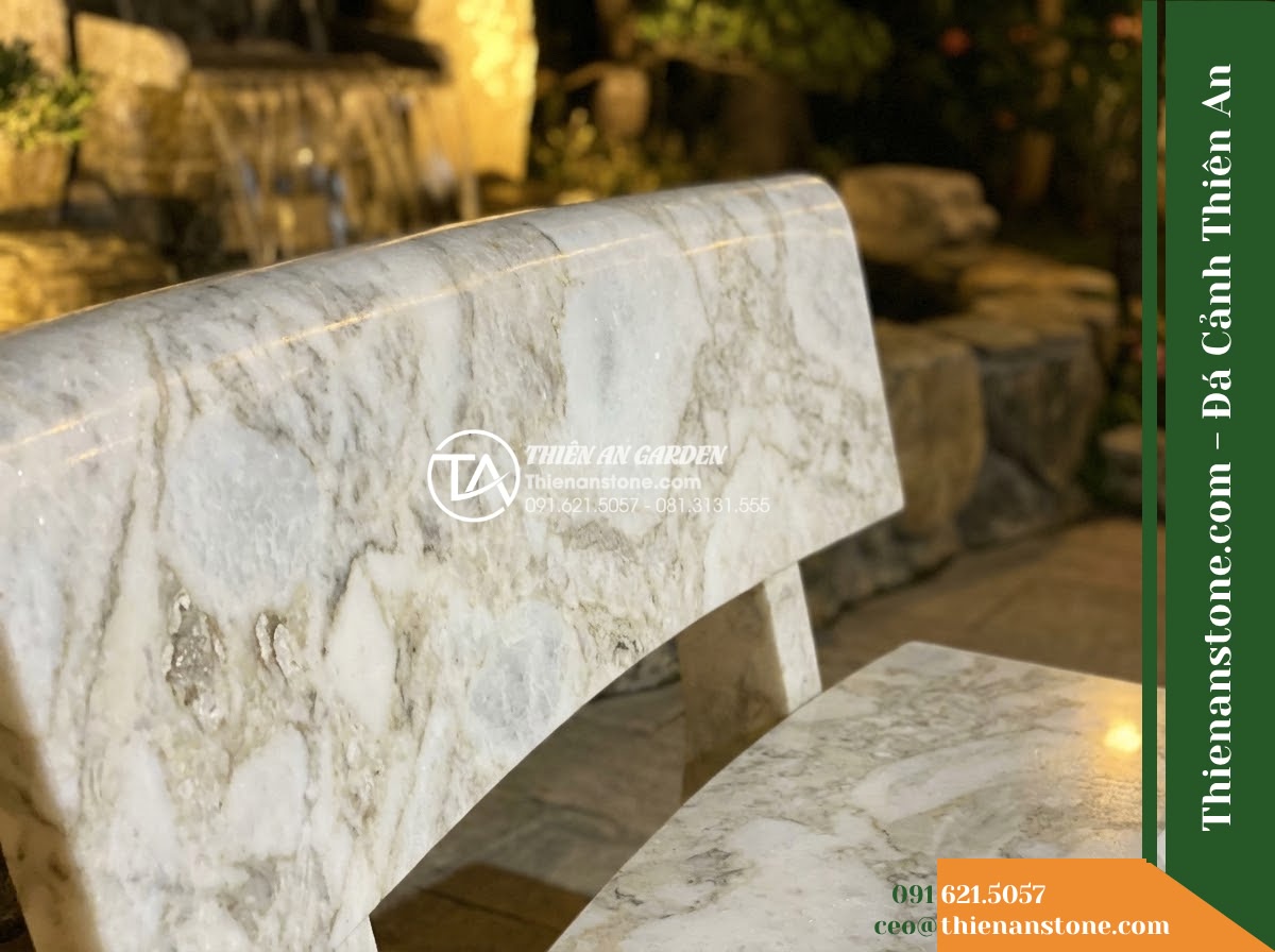 Ghế Đá Sân Trường Vững Bước – Kích thước 175 x 48 x 80 cm – Kiểu dáng tựa cong thấp, hai đầu vuông. Chất liệu đá vân mây - Hình 3 Ghế Đá Sân Trường Vững Bước – Kích thước 175 x 48 x 80 cm – Kiểu dáng tựa cong thấp, hai đầu vuông. Chất liệu đá vân mây - Stone bench of cloud marble beside a cascading water feature at night, illuminat