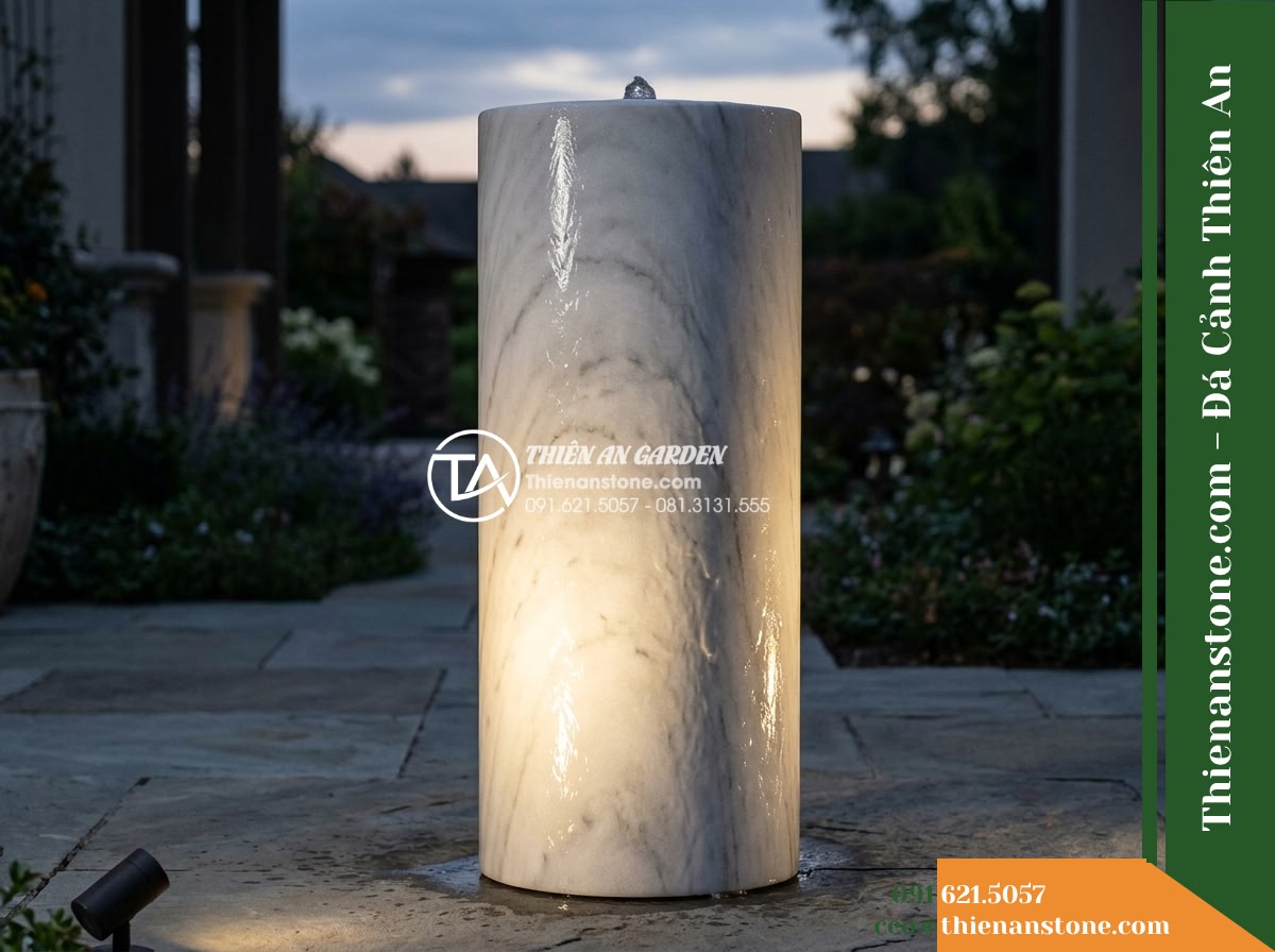 Trụ Phun Tròn Lỗ Xuyên Tâm, Mài Nhẵn D30cm Cao 80cm - Hình 13 Trụ Phun Tròn Lỗ Xuyên Tâm, Mài Nhẵn D30cm Cao 80cm - Dusk photograph showing the stone fountain illuminated by a low-angle raking spo