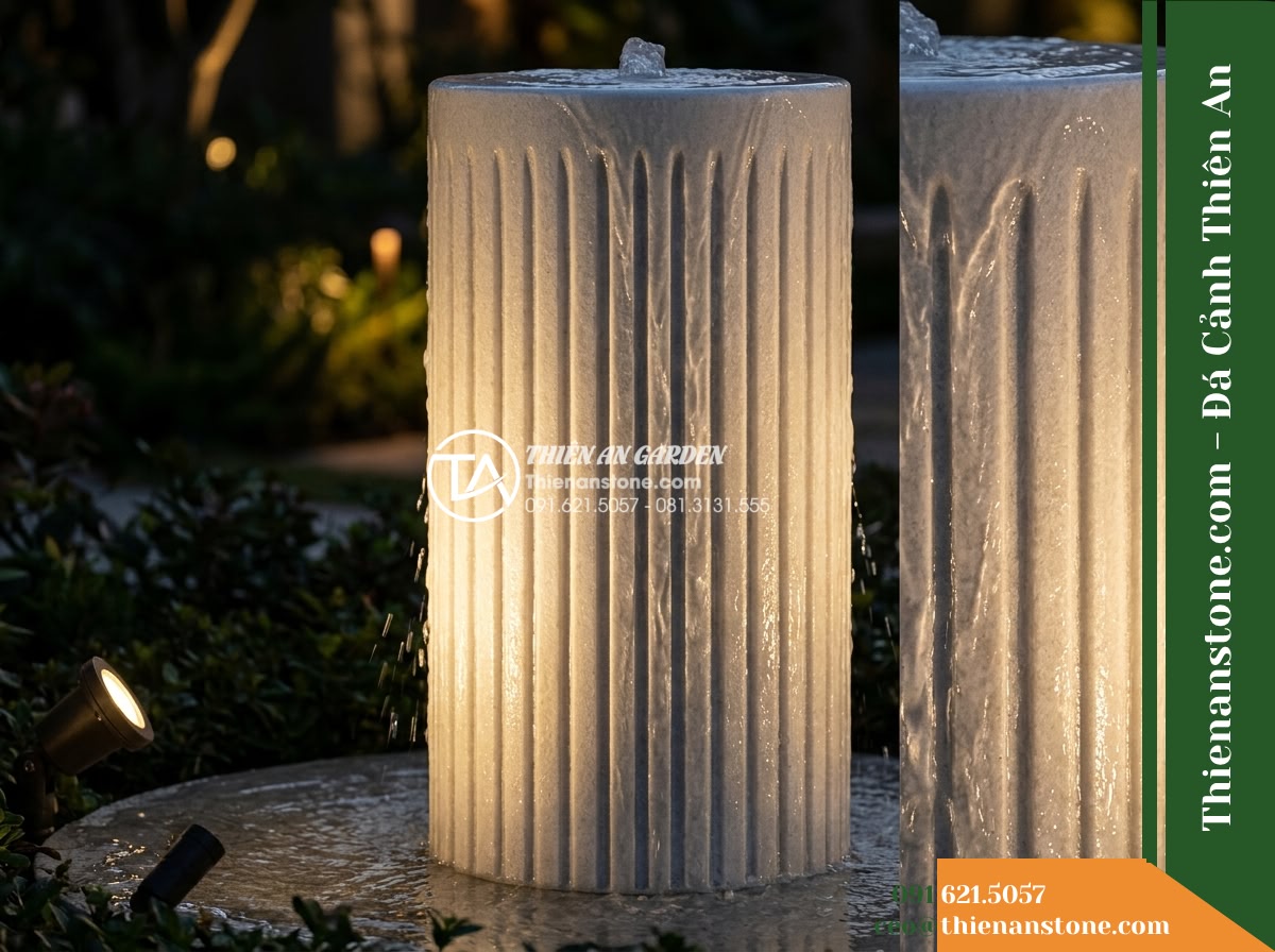 Trụ Phun Tròn Xẻ Rãnh Dọc Thân, Mài Mịn D35cm Cao 1m - Hình 14 Trụ Phun Tròn Xẻ Rãnh Dọc Thân, Mài Mịn D35cm Cao 1m - Evening ambiance view of the grooved stone pillar illuminated by a warm 3000K lo